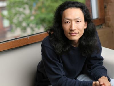 Sung J Woo sitting on a sofa in front of a window