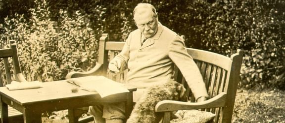 Arthur Conan Doyle writing outside on a bench.