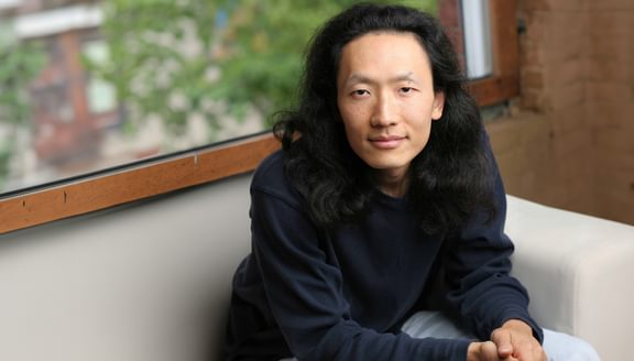 Sung J Woo sitting on a sofa in front of a window